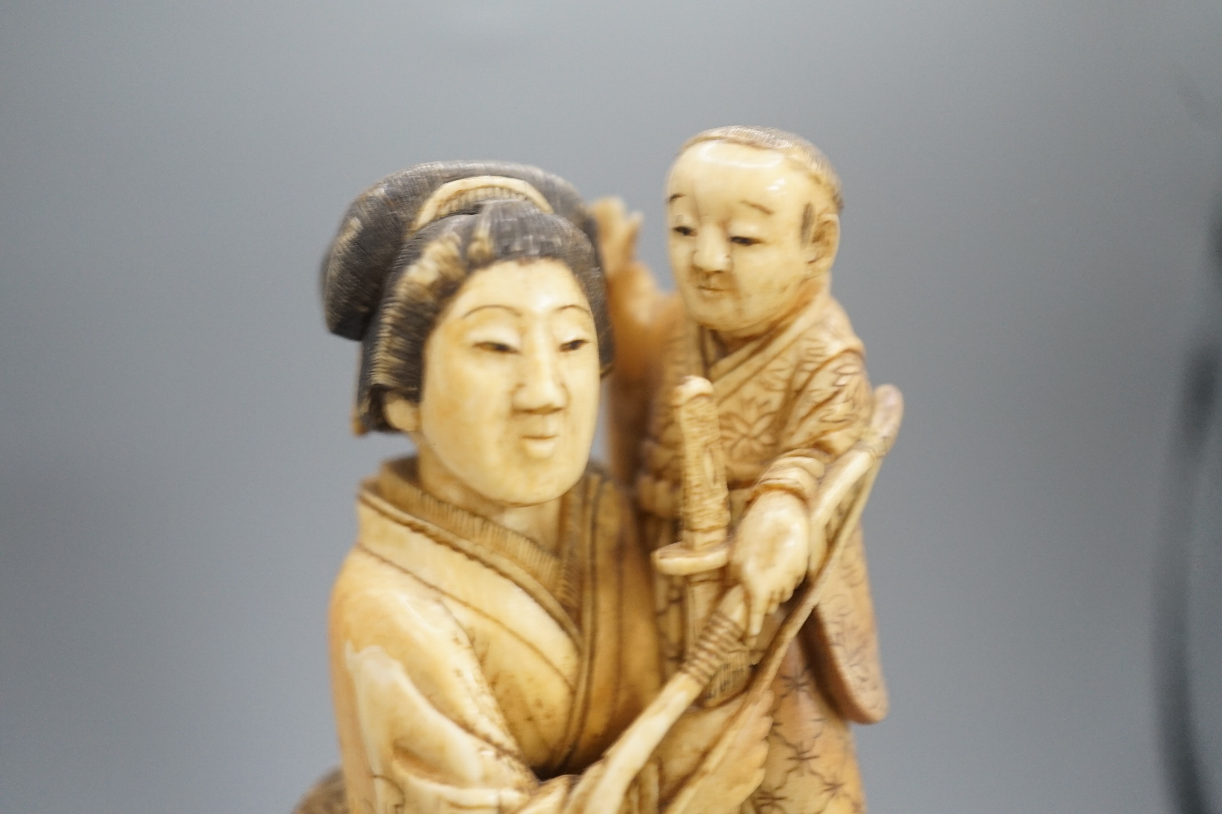 A Japanese ivory okimono of a lady holding a boy with a bow and arrow, Meiji period, restoration 12cm, wood stand